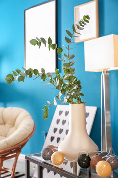 Vase with twigs and electric garland on table in living room