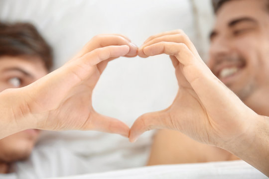 Young gay couple making heart symbol with their hands while lying in bed