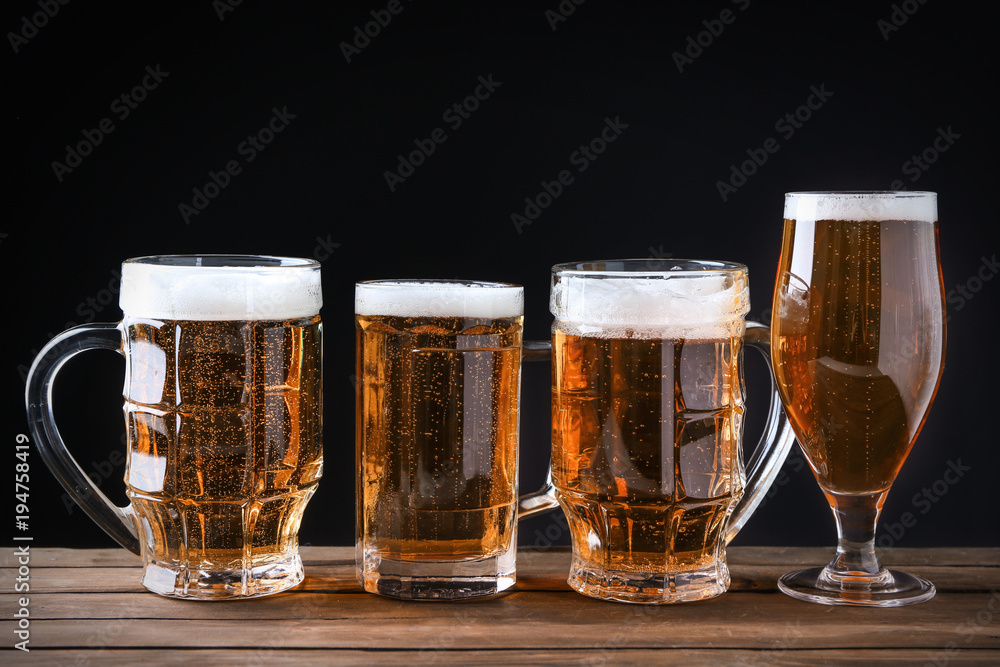 Wall mural Glassware with beer on wooden table against black background