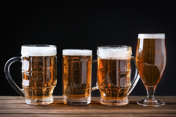 Glassware with beer on wooden table against black background