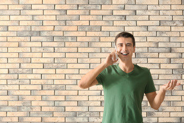 Young man talking on phone against brick wall background