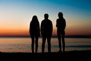 Silhouette of three friends in the morning at the beach looking at sunrise .