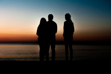 Silhouette of three friends in the morning at the beach looking at sunrise .