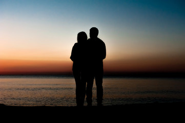 Silhouette of couple facing each other on the beach at sunrise.