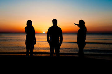 Silhouette of three friends in the morning at the beach looking at sunrise .