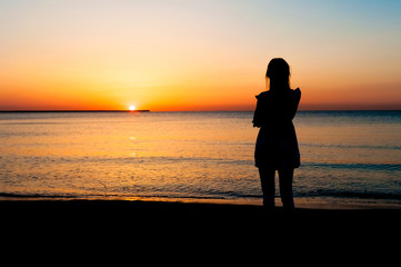 Fototapeta premium Woman in summer dress standing on a sandy beach and looking to the sun