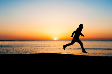 Fototapeta na wymiar Silhouette of man jumping in the air on the beach at sunrise.