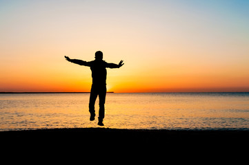 Silhouette of man jumping in the air on the beach at sunrise.