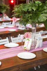 Decoration for a wedding ceremony on a back yard with tables, plates, and vases full of anthurium flowers and monstera leafs. Pink and green colors. Space for text