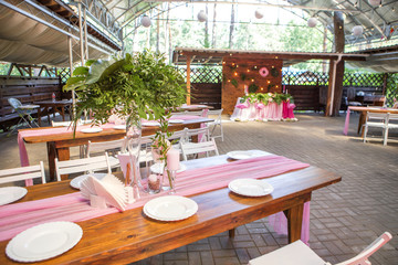 Decoration for a wedding ceremony on a back yard with tables, plates, and vases full of anthurium flowers and monstera leafs. Pink and green colors. Space for text