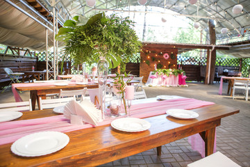 Decoration for a wedding ceremony on a back yard with tables, plates, and vases full of anthurium flowers and monstera leafs. Pink and green colors. Space for text
