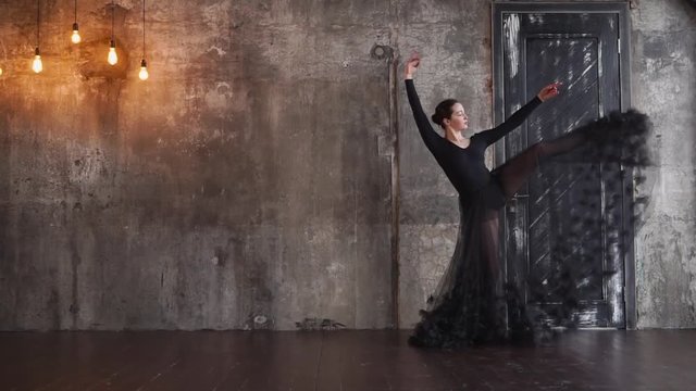 Amazing plastic woman is doing dancing steps in a gloomy room. She is lifting legs and swaying her skirt in rotating