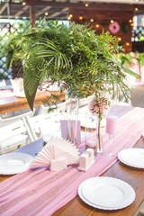 Decoration for a wedding ceremony on a back yard with tables, plates, and vases full of anthurium flowers and monstera leafs. Pink and green colors. Space for text