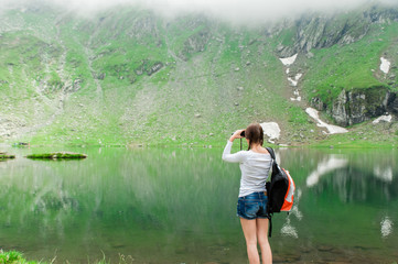 Young woman admiring the beautiful view of the lake and mountains, holding a binocular. Scene from Balea Lake, Romania.