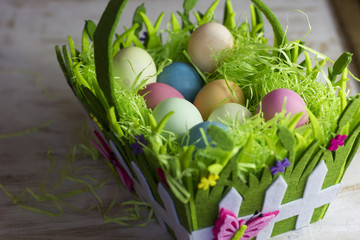 Colorful easter eggs in the decorative basket on a white wooden background