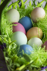 Colorful easter eggs in the decorative basket on a white wooden background