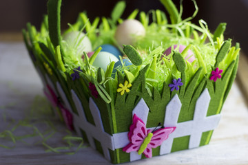 Colorful easter eggs in the decorative basket on a white wooden background