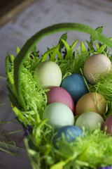 Colorful easter eggs in the decorative basket on a white wooden background