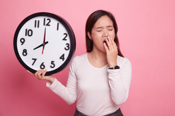 Sleepy young Asian woman with a clock in the morning.
