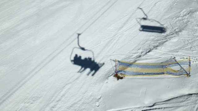 Shadow of ropeway ski lift with skiers moves upwards to top of mountain. Reflection on the snow