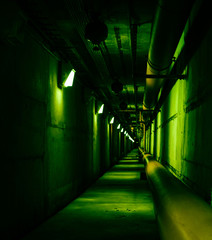 Psychedelic green deep in underground tunnel. Colored industrial background. Emergency lighting, row of fire extinguishers and tubes.