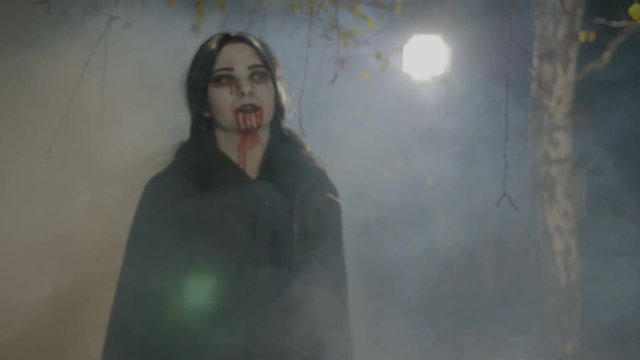 Thirsty young female vampire coming out from forest to hunt and showing her teeth on halloween night