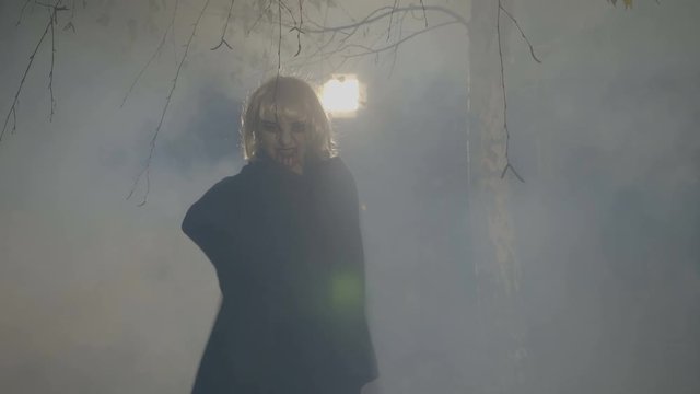 Blonde vampire uncovering his mantle and preparing to attack in the forest on halloween night