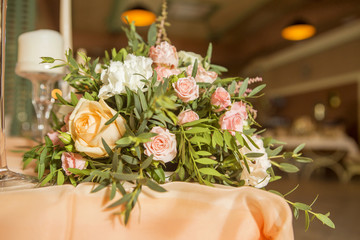 Wedding table decor full of rose and eustoma flowers, candles and peach colored fabric. Luxury rich restaurant interior. Indoor. Copy space