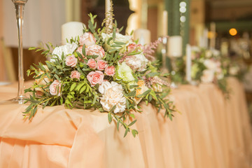 Wedding table decor full of rose and eustoma flowers, candles and peach colored fabric. Luxury rich restaurant interior. Indoor. Copy space