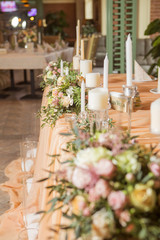 Wedding table decor full of rose and eustoma flowers, candles and peach colored fabric. Luxury rich restaurant interior. Indoor. Copy space
