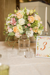 Wedding table decor full of rose and eustoma flowers, candles and peach colored fabric. Luxury rich restaurant interior. Indoor. Copy space