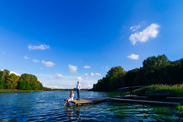 the couple on the pier of the lake admire of the sun and behind