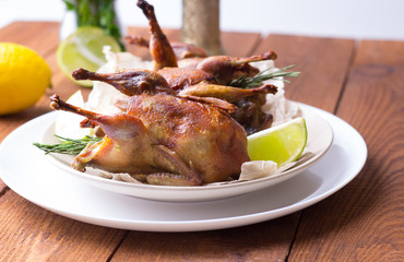 Appetizing baked quail with spices, herbs and lemon, lime in white dish on a wooden table