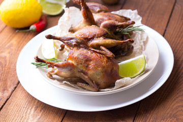 Appetizing baked quail with spices, herbs and lemon, lime in white dish on a wooden table