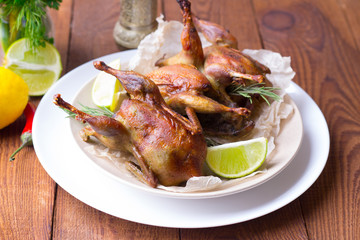 Appetizing baked quail with spices, herbs and lemon, lime in white dish on a wooden table