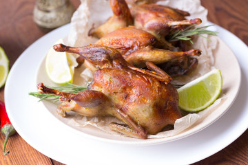 Appetizing baked quail with spices, herbs and lemon, lime in white dish on a wooden table