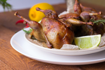 Appetizing baked quail with spices, herbs and lemon, lime in white dish on a wooden table