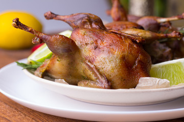 Appetizing baked quail with spices, herbs and lemon, lime in white dish on a wooden table