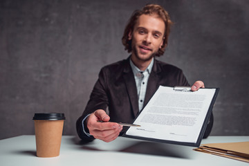 Portrait of cheerful unshaven man giving document and pen to affix signature. Conclusion of treaty...