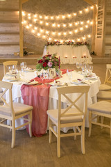 Set of wedding tables with wine color candles, plates and tablecloth surrounded by light garland and flowers. Interior. Copy space