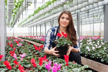 FYoung forists woman working with flowers in a greenhouse holding a pot smiling at camera