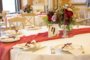 Set of glassess and plates on a wedding table surrounded by light garland and wine color flowers and tablecloth. Interior. Copy space
