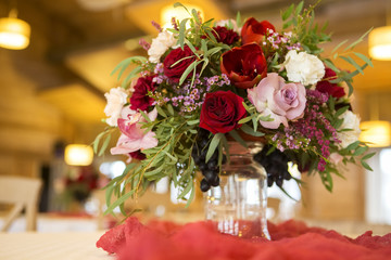 Wine color flowers on a wedding table surrounded by plates, tablecloths and candles. Interior. Copy space