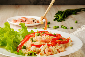Boiled rice with vegetables and fried shrimp on a lettuce on white plate and bamboo sticks. A healthy and tasty dish of chinese cuisine. Close-up view.