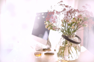 A bouquet of flowers in a round vase on a table by the window. A computer. Workplace at home. Background with bright colors. Spring bouquet7 Free space for text.