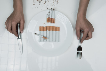 Top view of female hands taking cutlery from the table with plate full of cigarettes