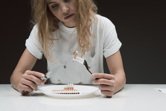 Depressed lady sitting in front of plate filled with rollups. She is staring at barbed ciggy pricked on fork. Isolated on background