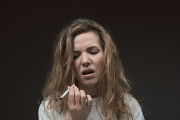 Portrait of peaceful female person standing with eyes closed from pleasure. She is holding cigarette. Isolated on background