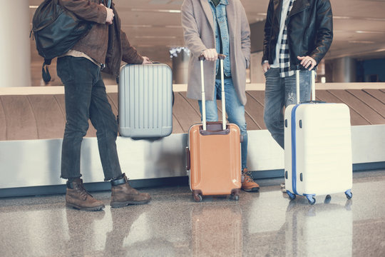 Three men situating near luggages while waiting for plane in hall. Expectation and tourism concept