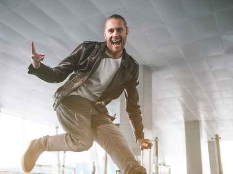 Portrait of cheerful unshaven male jumping in hall. He leaning on baggage. Entertainment concept